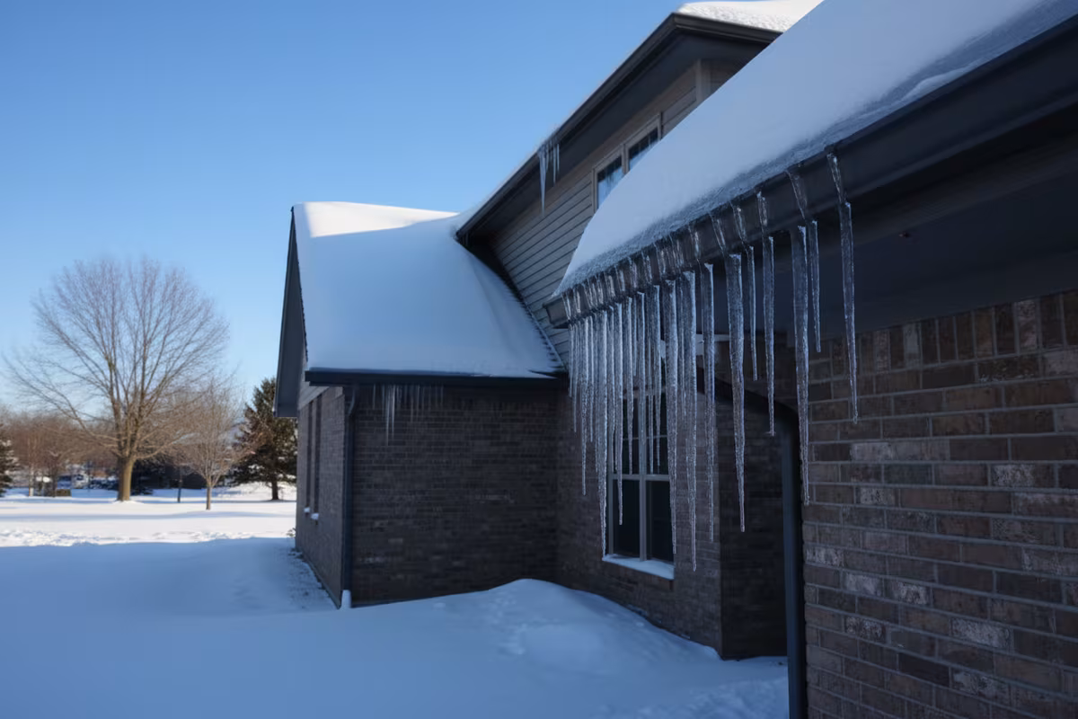 Ice dam with long icicles hanging from a clogged gutter on a Rockford Illinois home in winter